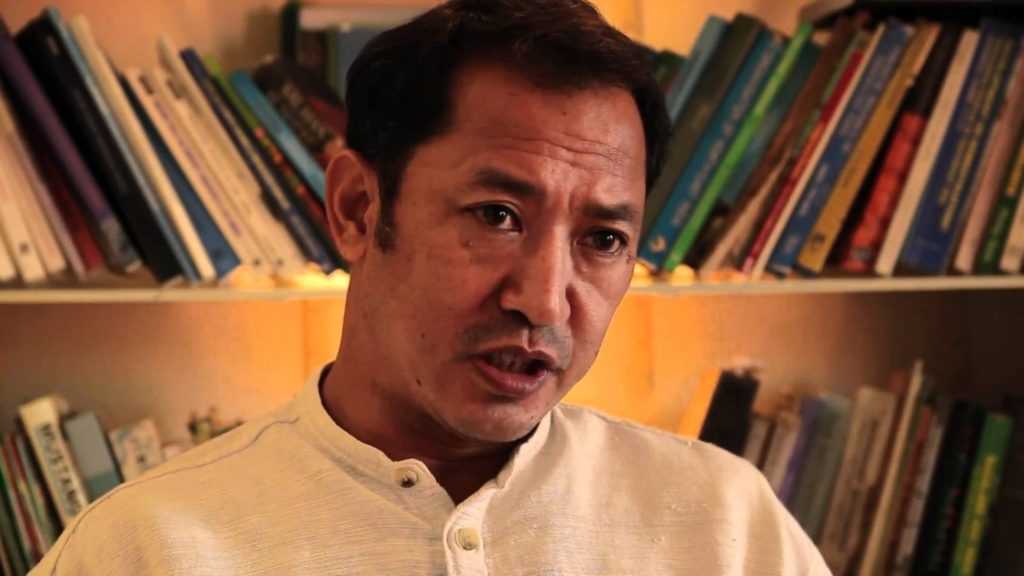 চাকমা সার্কেল চিফ রাজা দেবাশীষ রায় — সাদা পাঞ্জাবি পরে কথা বলছেন, পেছনে বইয়ে ঠাসা তাক
