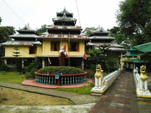 বহু ধাপে ওঠা ছাদের কারুকাজ করা বৌদ্ধ বিহার, সামনে গোলাকার বাগান ও সাদা সিংহমূর্তি