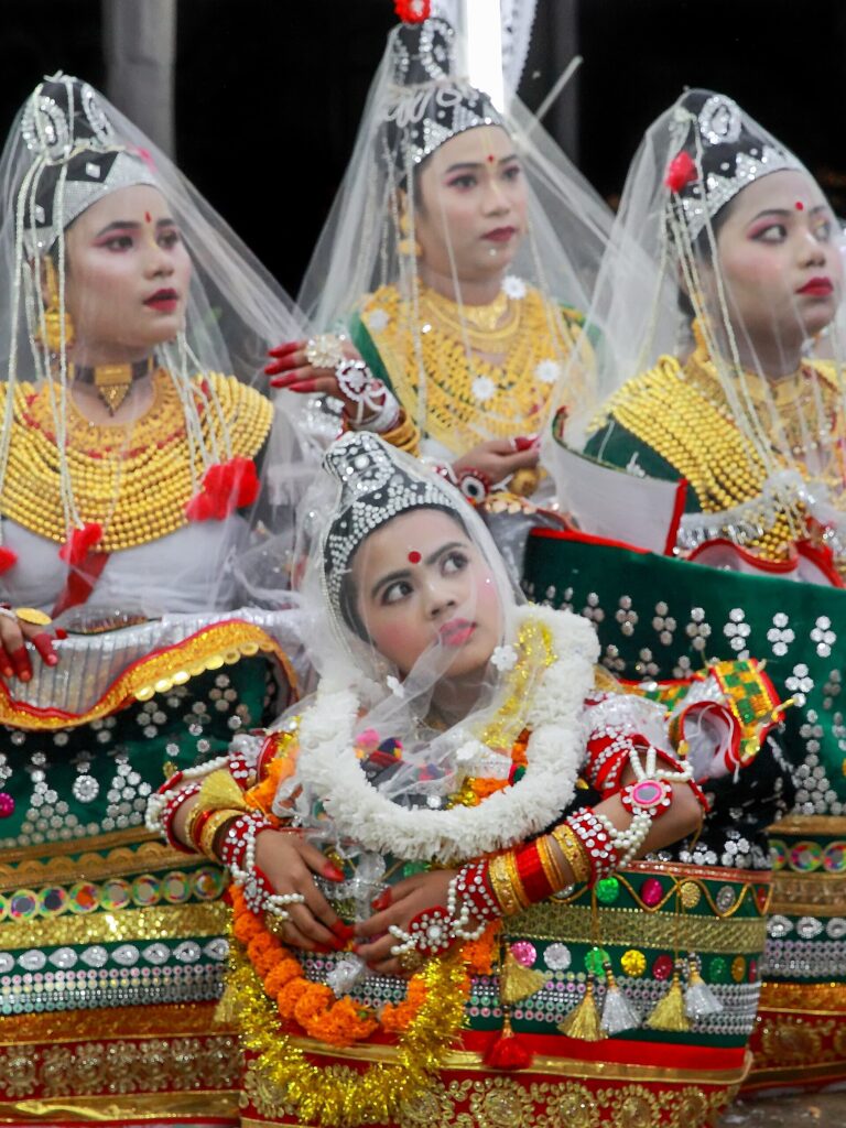ঐতিহ্যবাহী মণিপুরী পোশাকে কয়েকজন নৃত্যশিল্পী, মাথায় সাদা ওড়না ও চূড়া, গলায় সোনালি গয়না ও ফুলের মালা