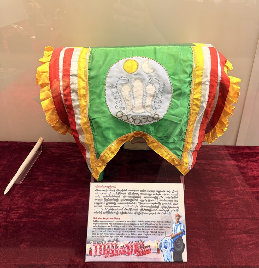 লাল কাপড়ে ঢাকা টেবিলে রাখা রাখাইন ঐতিহ্যবাহী ঢাক, সবুজ-হলুদ-লাল কাপড়ে মোড়া আর সামনে বর্ণনার ফলক