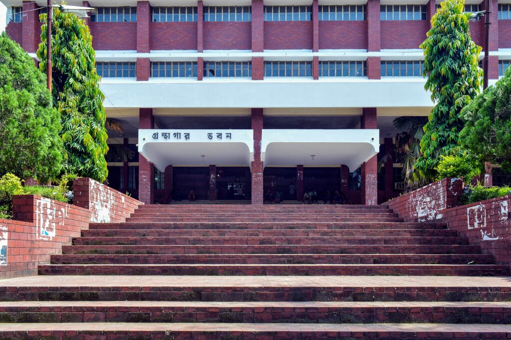 চট্টগ্রাম বিশ্ববিদ্যালয়ের লাল ইটের গ্রন্থাগার ভবন — চওড়া সিঁড়ির ওপরে প্রবেশপথে বাংলায় লেখা 'গ্রন্থাগার ভবন', দুপাশে সবুজ গাছ