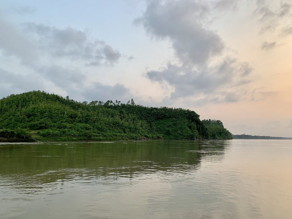 রাঙ্গুনিয়ার কাছে কর্ণফুলী নদী, নদীর পাড়ে সবুজ গাছে ঢাকা টিলা আর মেঘলা সন্ধ্যার আকাশ
