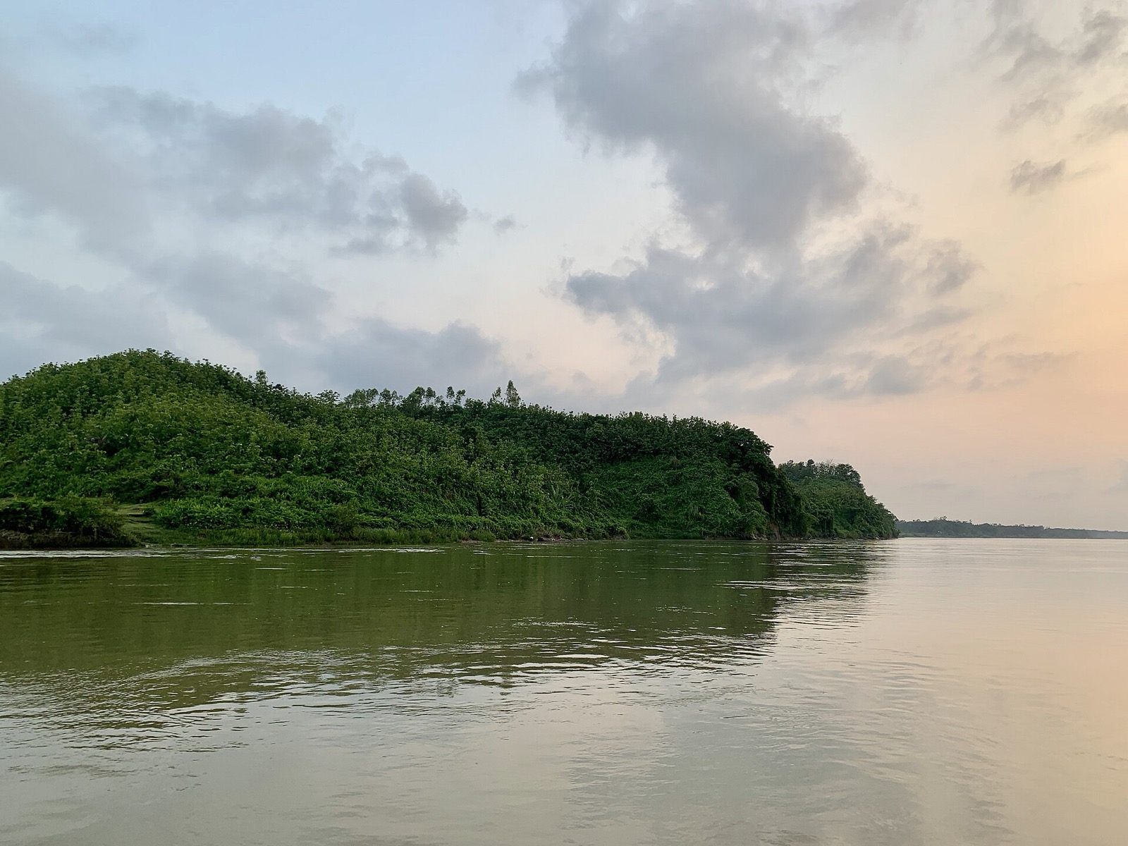 রাঙ্গুনিয়ার কাছে কর্ণফুলী নদী, নদীর পাড়ে সবুজ গাছে ঢাকা টিলা আর মেঘলা সন্ধ্যার আকাশ