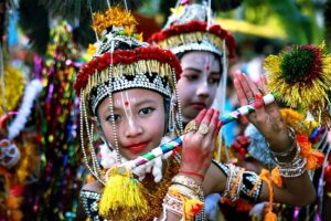 রাস উৎসবে মুকুট, পুঁতির মালা ও জরির সাজে কৃষ্ণ বেশে দুটি শিশু, একজনের হাতে রঙিন বাঁশি; পেছনে ঝলমলে সাজসজ্জা
